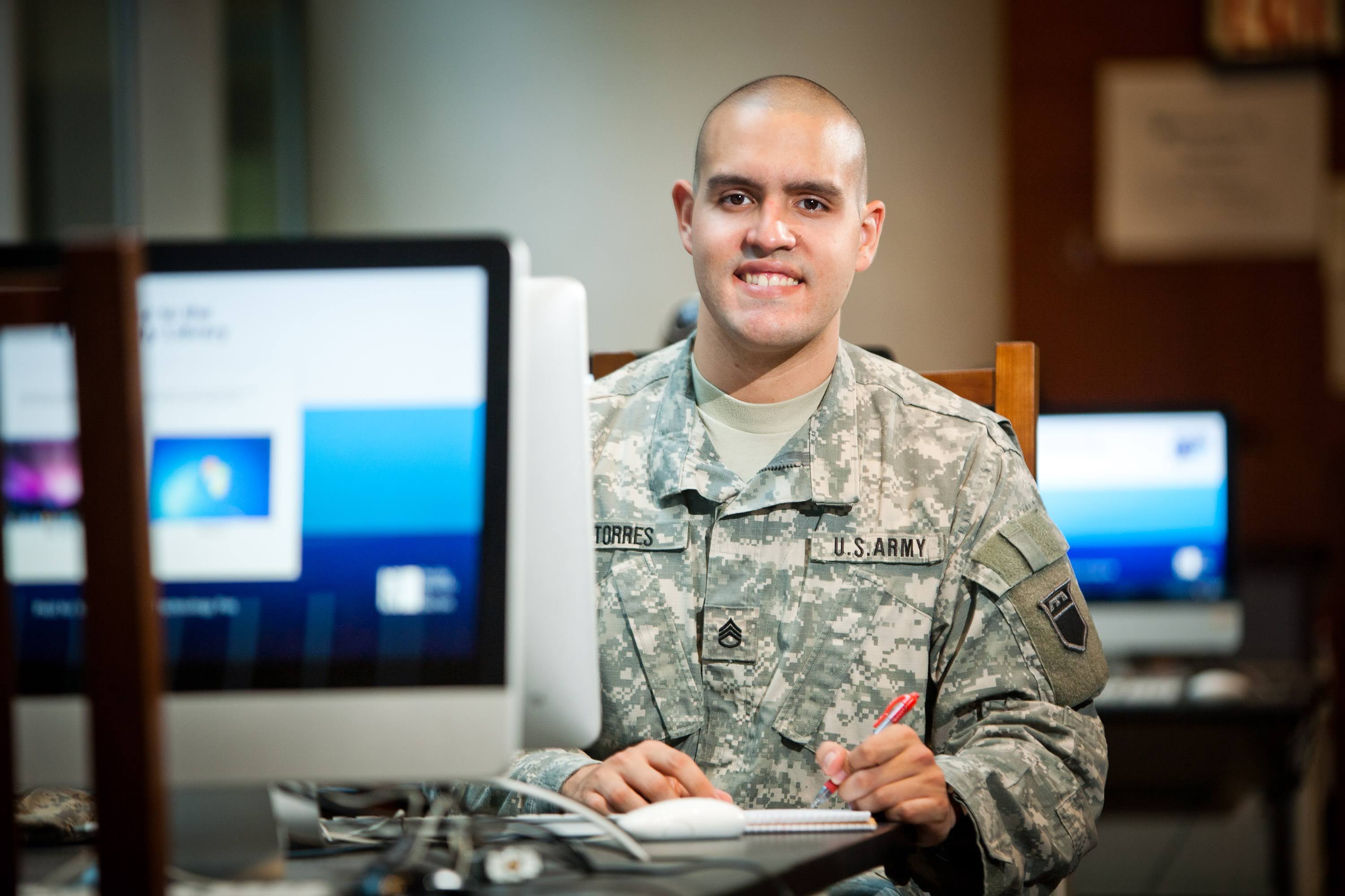 Young man in U.S. Army uniform sitting and working behind a computer