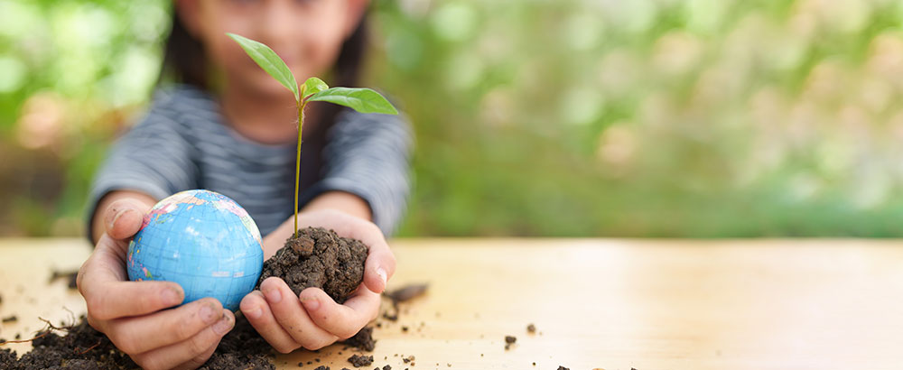 child holding world in one hand and small plant in the other